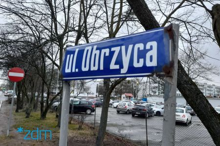 Stara tablica z nazwą ulicy Obrzyca zawieszona przy parkingu