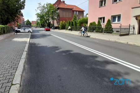 Ulica Polna po remoncie. Po lewej stronie chodnik. Na środku nowa jezdnia na której jedzie samochód i rower. Po prawej stronie budynek mieszkalny