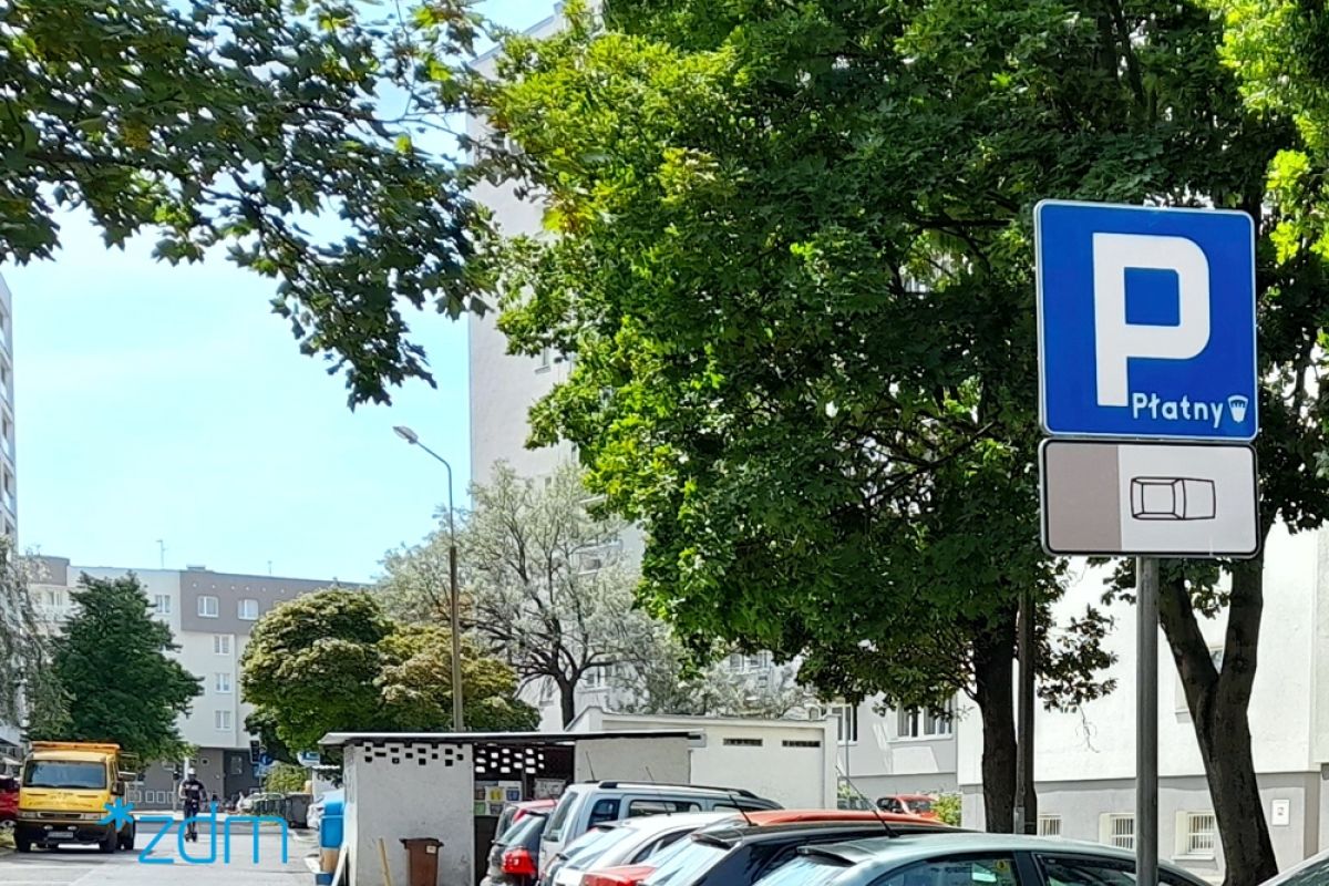 Po lewej stronie znak informujący o płatnym parkowaniu. Za nim zaparkowane samochody. Po prawej ulica Barzyńskiego