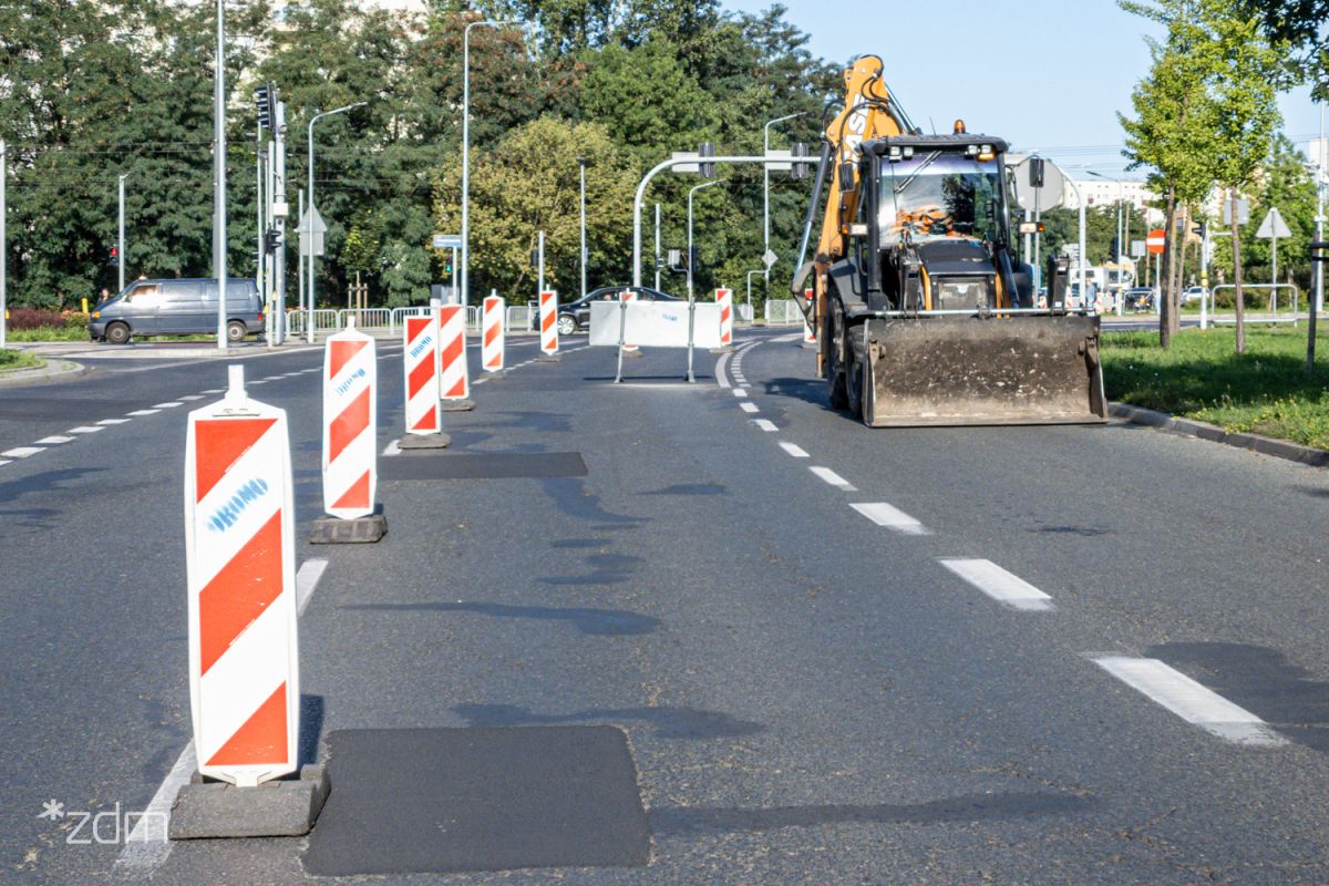 po lewej stronie pachołki wygradzające pasy ruchu, po prawej stronie koparka