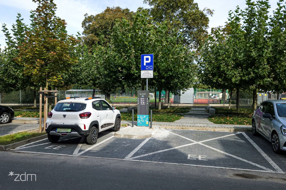 po lewej stronie samochód elektryczny zaparkowany przy stacji ładowania pojazdów elektrycznych po prawej pusta koperta dla samochodu elektrycznego