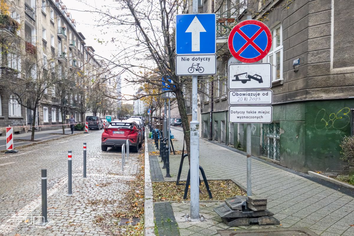 Znak zakazu zatrzymywania się z tabliczką o odholowywaniu pojazdów. Za nimi zaparkowane samochody