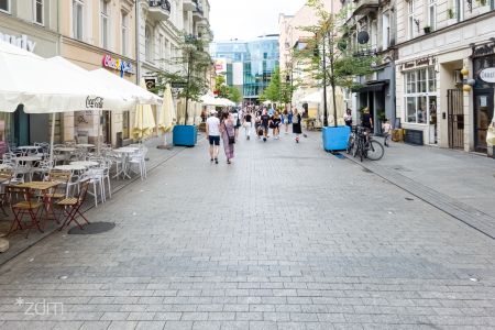 Ulica Wrocławska, po obu stronach elewacje kamienic. Po lewej stoliki i krzesła ogródków gastronomicznych.