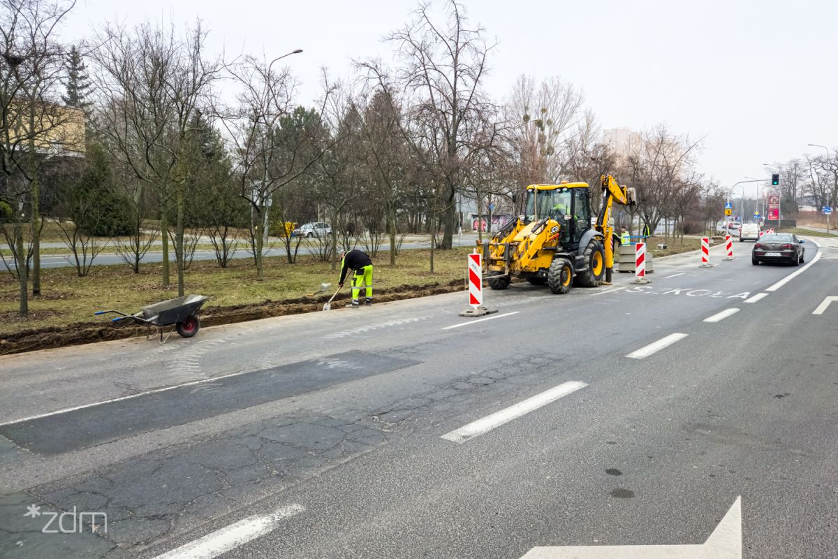 Zniszczona nawierzchnia jezdni, pracujący robotnicy i koparka