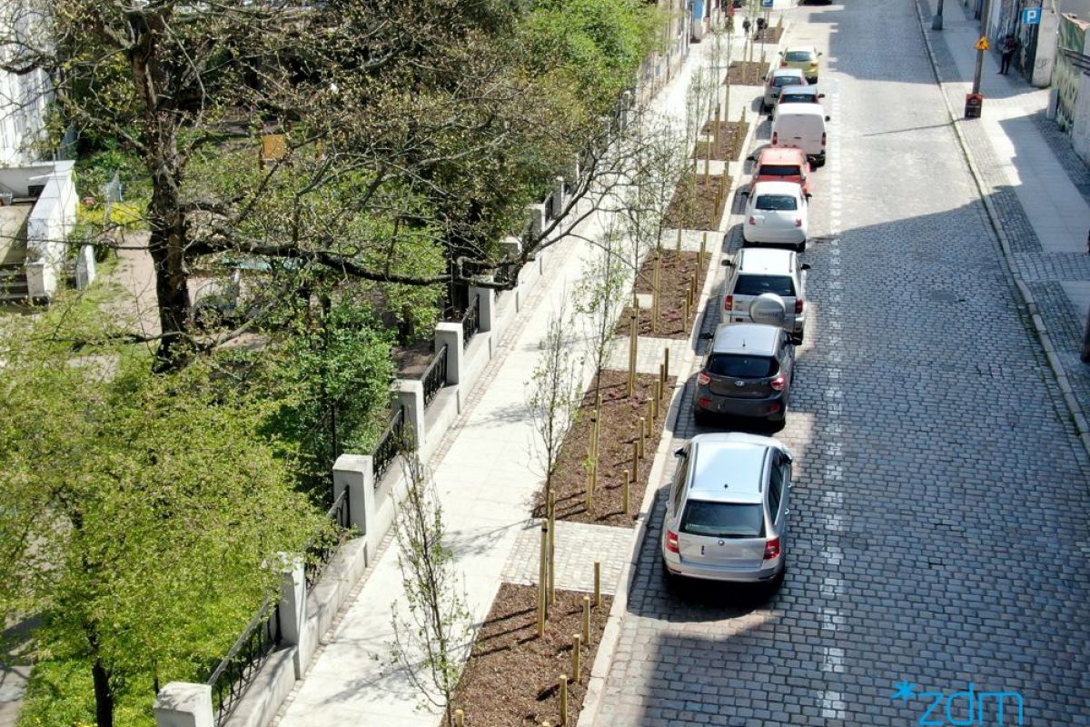 Zdjęcie z drona. Po lewej stronie zieleń, następnie wremontowany chodnik. Pasy zieleni z nowymi drzewami. Po prawej stronie jezdnia z zaparkowanymi samochodami