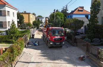 Czerwona ciężarówka podczas rozładunku na ul. Radosnej, wokół domy i ogródki jednorodzinne