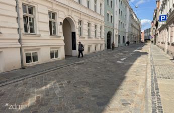 Widok na jezdnię na ulicy Za Bramką wraz z kamienicą po lewej stronie i oznakowaniem informacyjnym po prawej