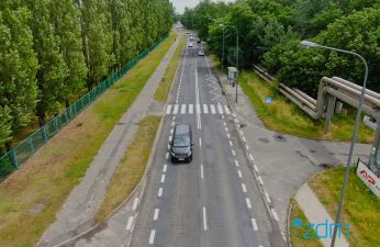 Ulica Strzeszyńska z lotu ptaka. Jezdnia, po lewej stronie chodnik i pas zieleni z drzewami. Po prawej przystanek autobusowy i zieleń.
