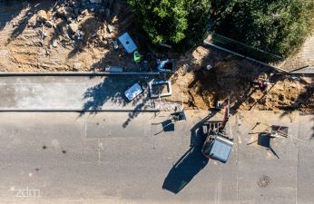 widok z drona na budowany chodnik, po prawej stronie pracownicy i koparka