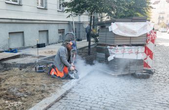 Robotnik klęczy przy krawężniku na remontowanym chodniku
