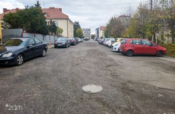 po lewej zaparkowane samochody centralnie gruntowa jezdnia po prawej zaparkowane samochody