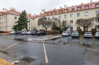 widok na plac, na pierwszym planie wyznaczone tymczasowe przejście dla pieszych, na drugim zaparkowane pojazdy i budynek mieszkalny