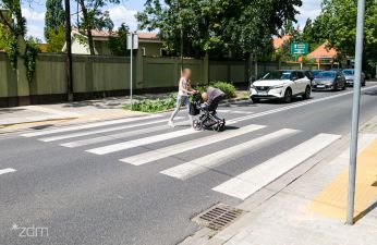 Przejście dla pieszych przez które przechodzi kobieta z wózkiem dziecięcy, w tle biały samochód 