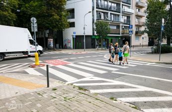 Przejście dla pieszych, z lewej biały bus i ludzie na środku przejścia 