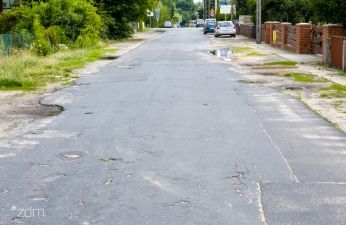 Nawierzchnia jezdni ulicy Krokusowej, w tle po prawej stronie płot oraz dalej zaparkowane auta