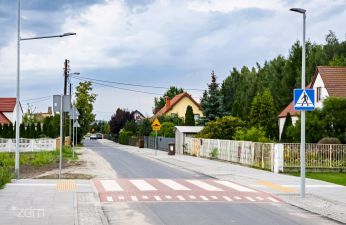Ulica Garaszewo z chodnikiem, przejściem dla pieszych z oświetleniem, w tle po prawej stronie widać dwa domy, po lewej jeden