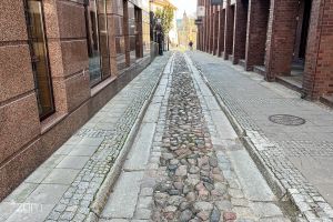 Bo bokach ściany z czerwonej cegły, na środku wąska brukowana ulica