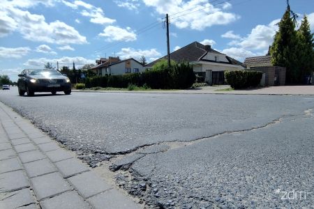 Zniszczona nawierzchnia jezdni, na niej jadący samochód