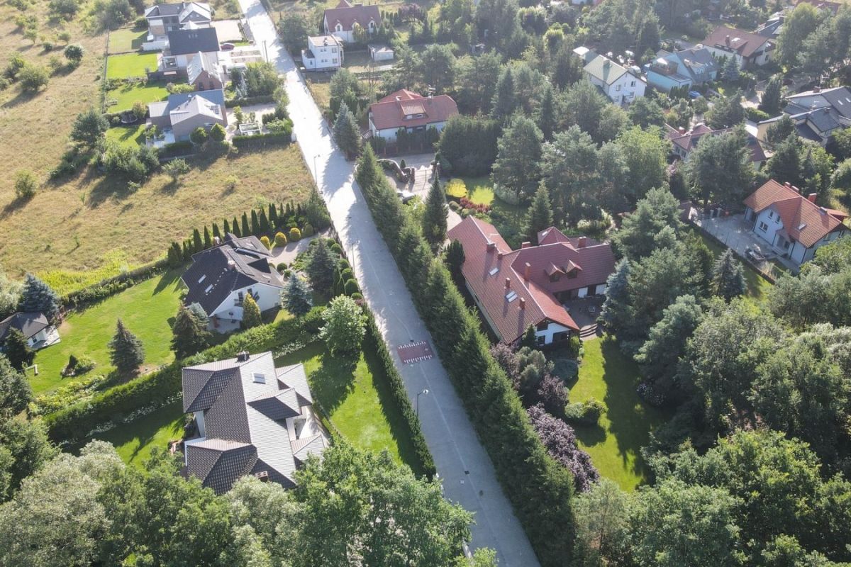 Ulica Mleczowa. Zdjęcie wykonane z drona. Po bokach zieleń i domki, na środku nitka ulicy