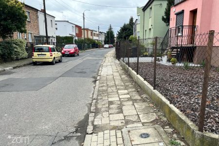 Zniszczony chodnik i jezdnia, w tle zabudowa jednorodzinna