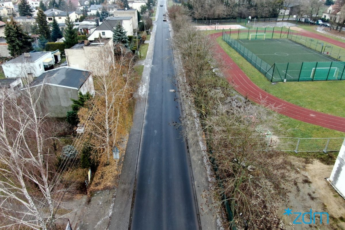 Ulica Baranowska po remenocie. Zdjęcie z drona, Od lewej domki jednorodzinne, na środku jezdnia, a po prawej stronie boisko sportowe