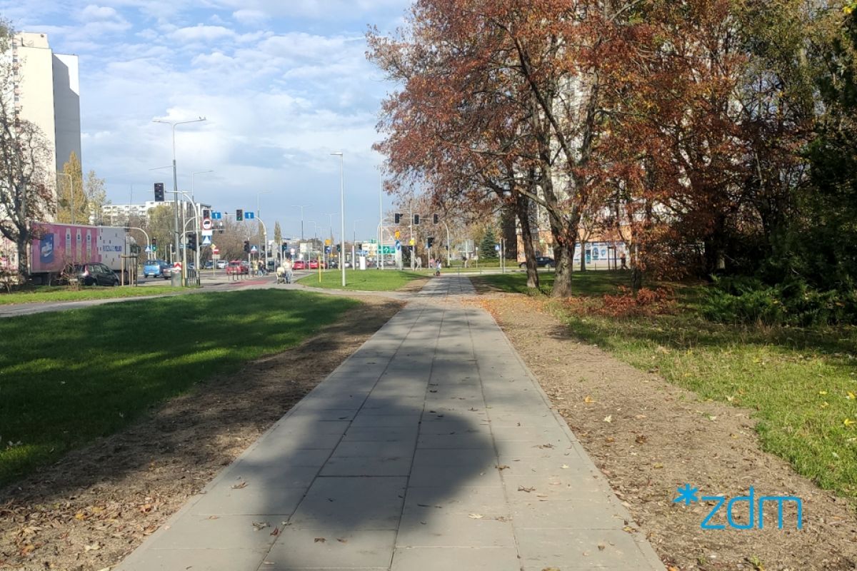 Trawnik z lewej strony, na głonym planie nowy chodnik, po prawej drzewa i zieleń
